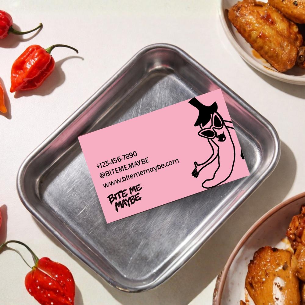Overhead view of a silver takeout tray containing a Bite Me Maybe sauce packet, fried chicken, and a business card.
