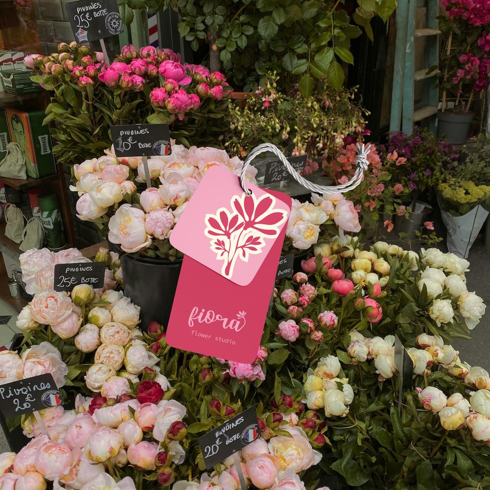 Close-up of fresh pink peonies featuring a branded pink Fiora hang tag with a white floral logo.