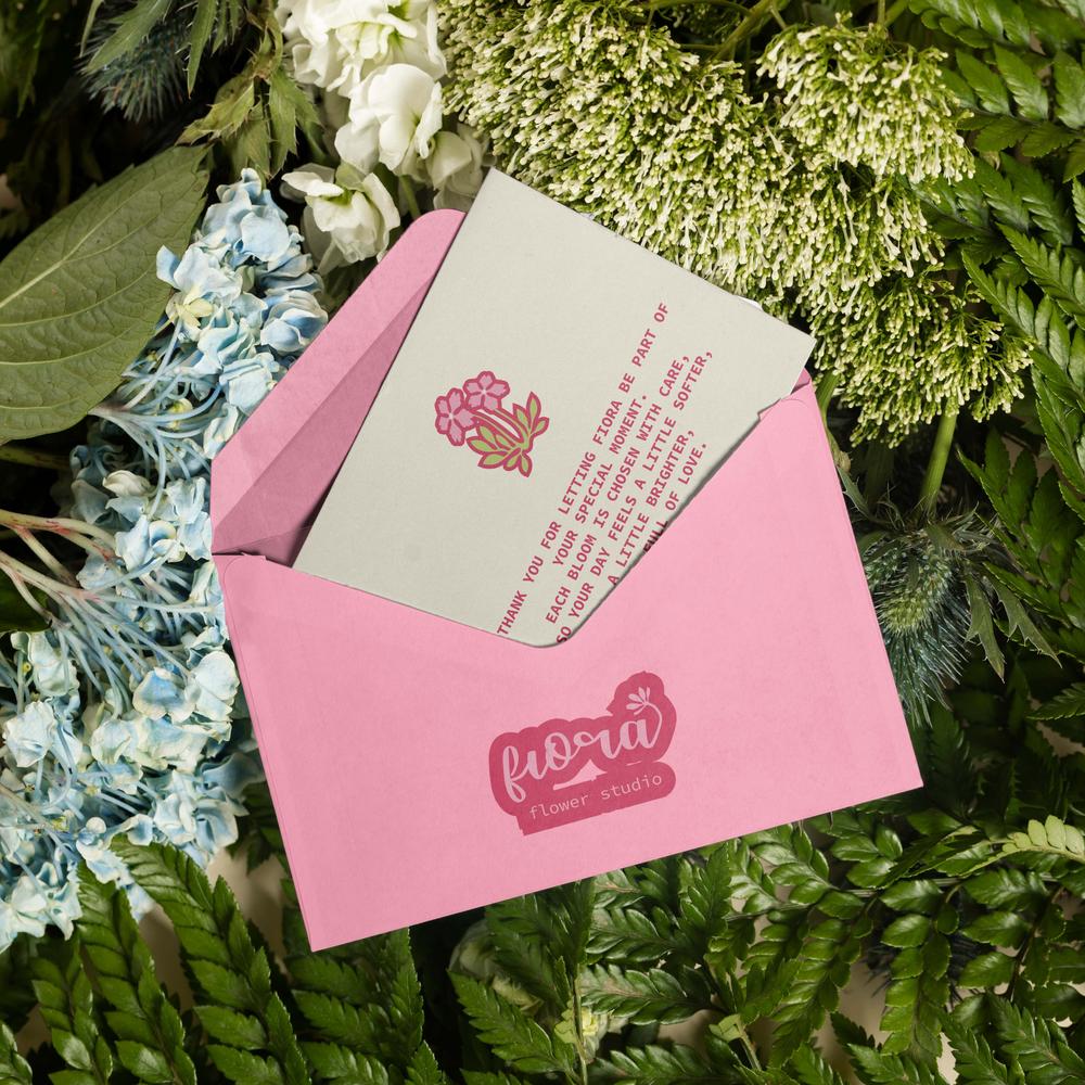 An open pink envelope resting on ferns, revealing a "Thank You" card with a red floral illustration.
