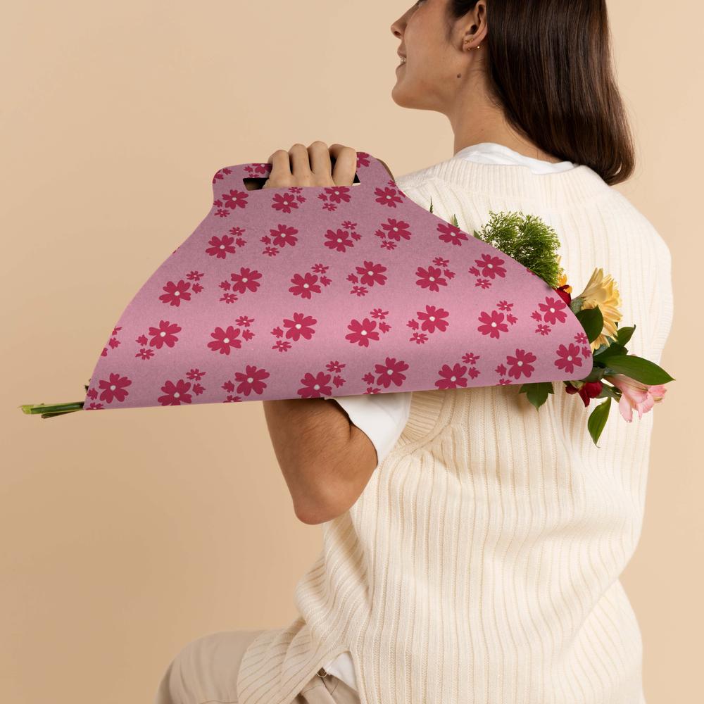 A woman holding a pink floral-patterned bouquet carrier designed to look like a fashionable clutch bag.