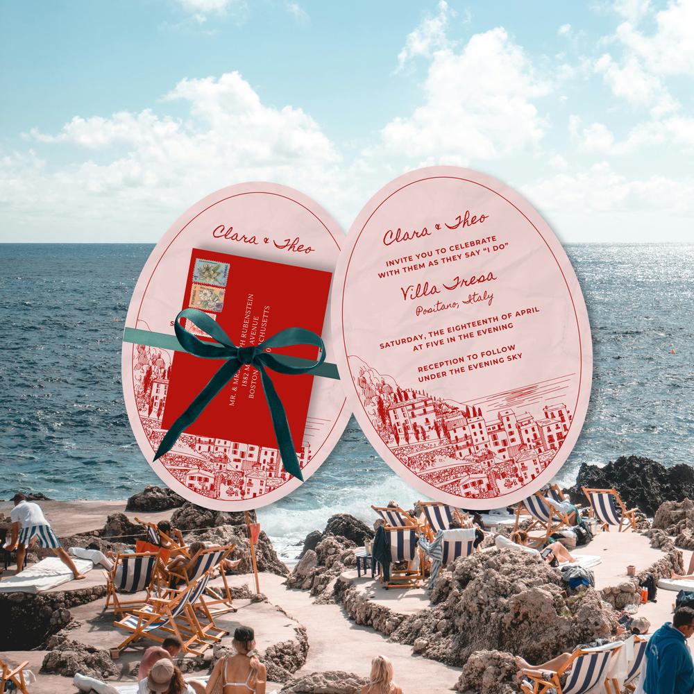 Hand holding round Mediterranean wedding invitations against a blurred Italian coastal view.